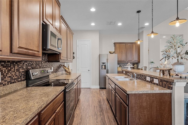 kitchen with decorative backsplash, pendant lighting, sink, stainless steel appliances, and hardwood / wood-style flooring