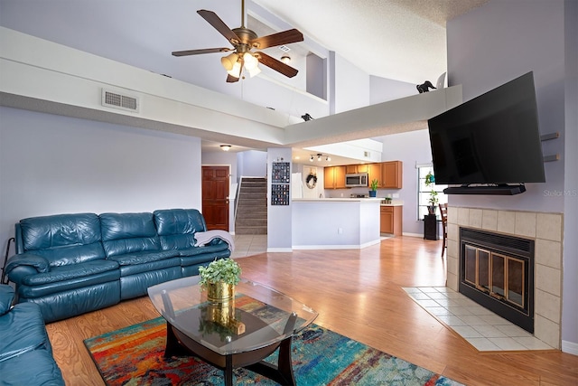 living room with a tile fireplace, ceiling fan, high vaulted ceiling, light hardwood / wood-style floors, and a textured ceiling