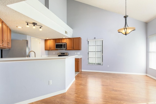 kitchen with sink, hanging light fixtures, stainless steel appliances, high vaulted ceiling, and light wood-type flooring