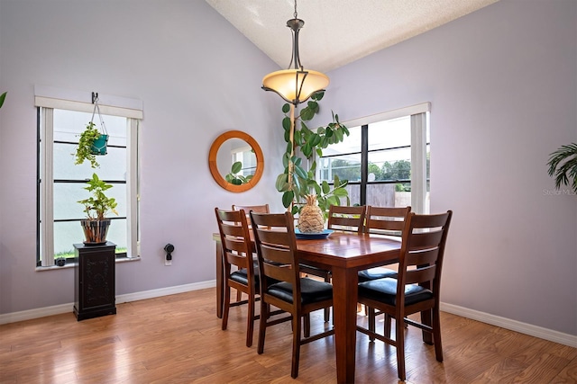 dining area with wood-type flooring, high vaulted ceiling, and a textured ceiling