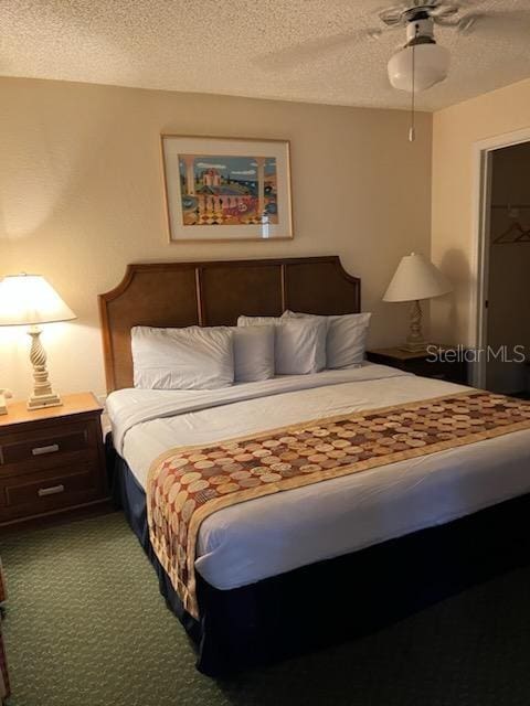 carpeted bedroom featuring ceiling fan, a textured ceiling, a closet, and a walk in closet