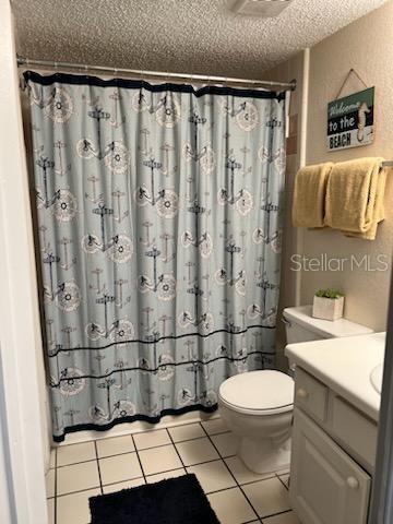 bathroom featuring tile patterned flooring, a textured ceiling, walk in shower, vanity, and toilet