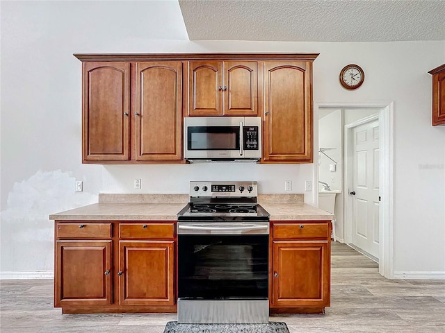 kitchen with a textured ceiling, light hardwood / wood-style flooring, and appliances with stainless steel finishes