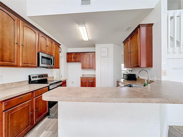 kitchen featuring stainless steel appliances, sink, kitchen peninsula, a textured ceiling, and light hardwood / wood-style flooring