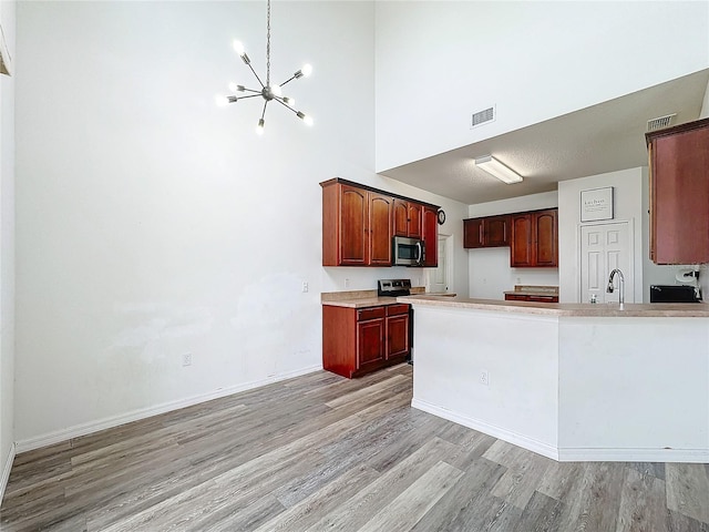 kitchen with stainless steel appliances, a towering ceiling, light hardwood / wood-style flooring, and a notable chandelier