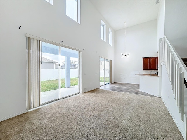 unfurnished living room featuring light colored carpet, high vaulted ceiling, and a notable chandelier