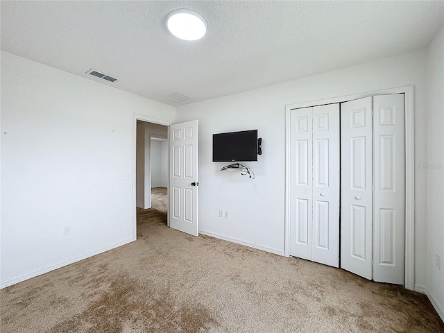 unfurnished bedroom featuring a closet, a textured ceiling, and light carpet