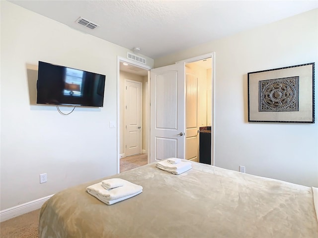 bedroom with light colored carpet, a textured ceiling, and ensuite bathroom