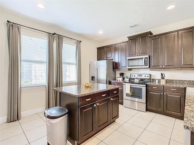 kitchen with light stone counters, appliances with stainless steel finishes, light tile patterned floors, and dark brown cabinetry