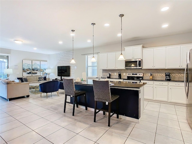 kitchen with white cabinets, a center island with sink, a breakfast bar area, appliances with stainless steel finishes, and decorative light fixtures