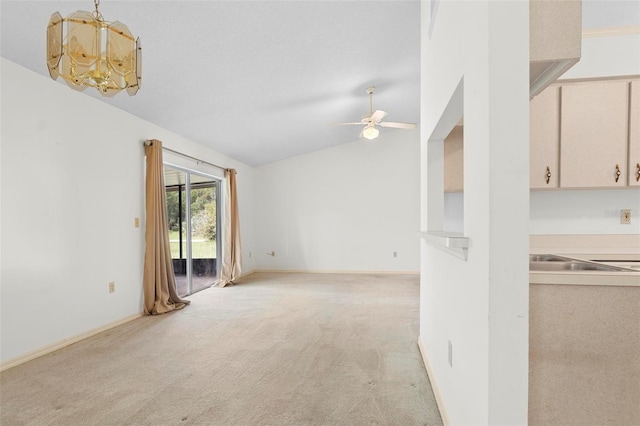 unfurnished living room featuring ceiling fan with notable chandelier, vaulted ceiling, and light carpet