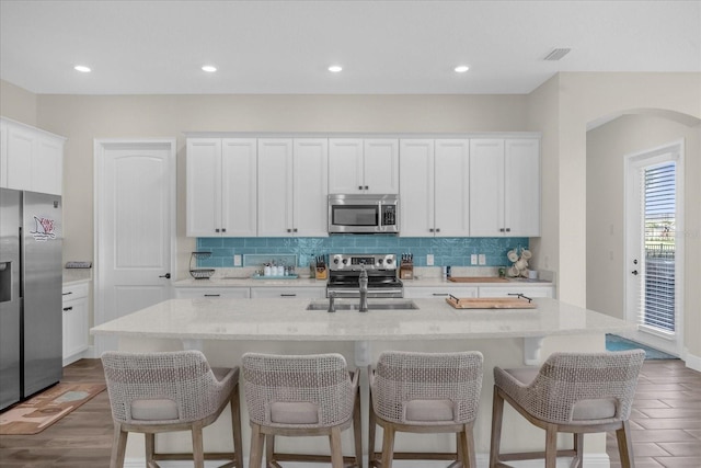 kitchen featuring dark hardwood / wood-style flooring, light stone counters, stainless steel appliances, white cabinets, and an island with sink