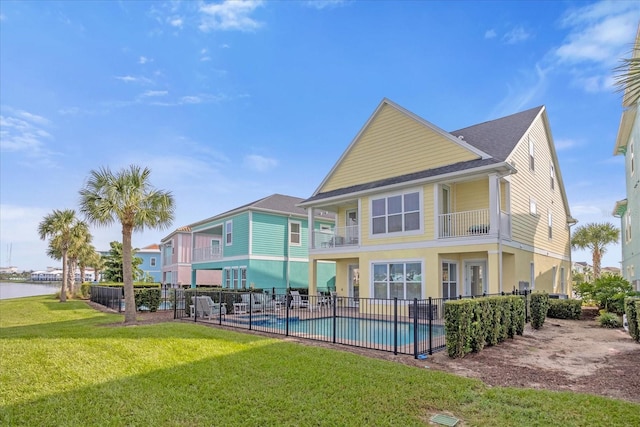 back of house with a fenced in pool, a water view, a yard, and a balcony