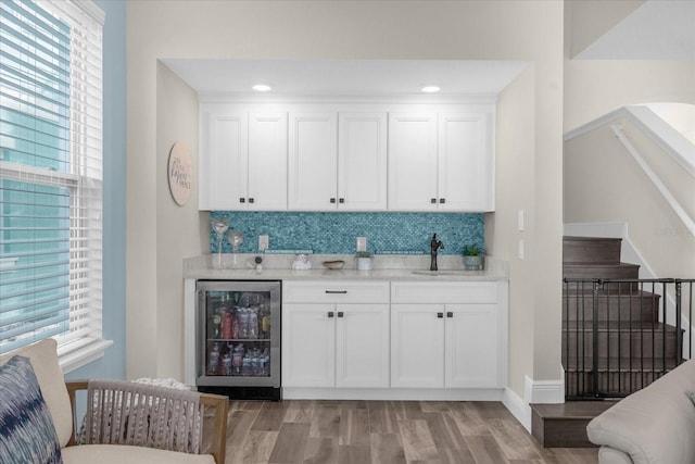 bar with backsplash, sink, wine cooler, light hardwood / wood-style flooring, and white cabinetry