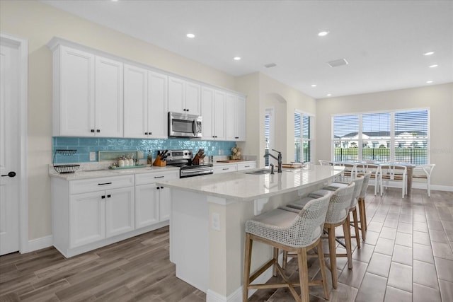 kitchen featuring appliances with stainless steel finishes, light stone counters, sink, a center island with sink, and white cabinetry