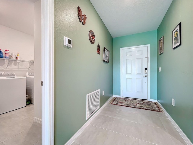 doorway to outside with washer and dryer, a textured ceiling, and light tile patterned flooring