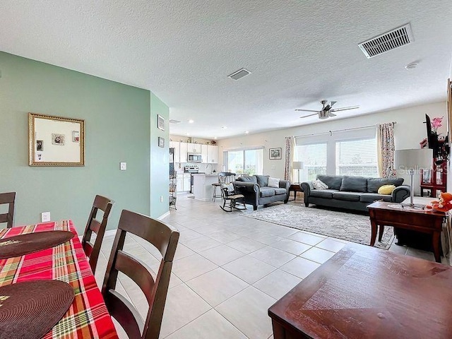 living room with a textured ceiling, ceiling fan, and light tile patterned floors