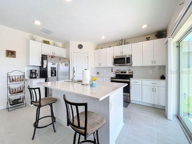 kitchen with white cabinetry, stainless steel appliances, a kitchen bar, and an island with sink