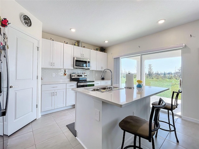 kitchen featuring a kitchen island with sink, a breakfast bar area, stainless steel appliances, sink, and white cabinetry