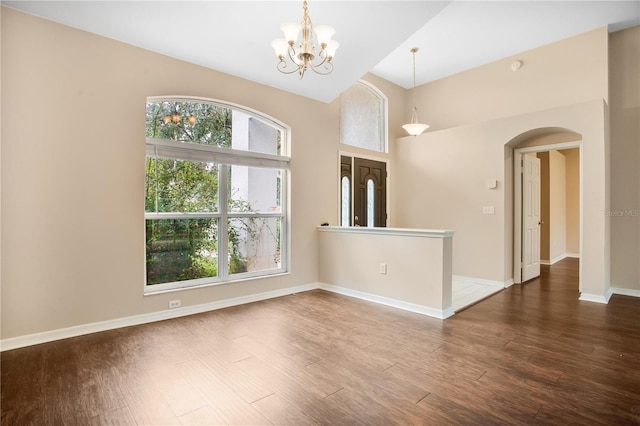 spare room with a towering ceiling, wood-type flooring, and an inviting chandelier