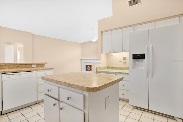 kitchen with white appliances, light tile patterned floors, a kitchen island, and white cabinets