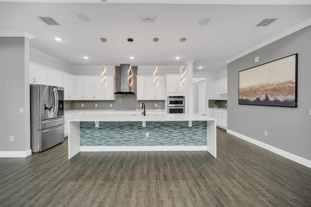 kitchen featuring appliances with stainless steel finishes, dark wood-type flooring, white cabinets, pendant lighting, and wall chimney range hood