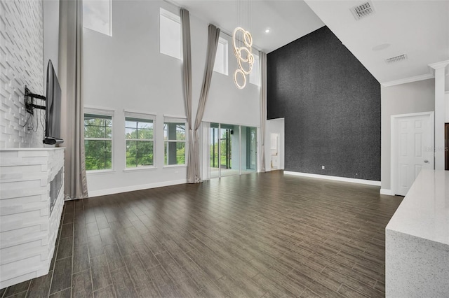 unfurnished living room featuring a towering ceiling, a fireplace, dark hardwood / wood-style flooring, ornamental molding, and a notable chandelier