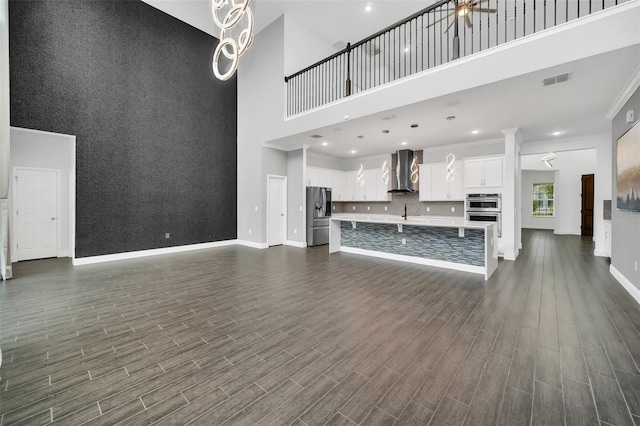 unfurnished living room featuring a towering ceiling, ceiling fan, crown molding, and dark hardwood / wood-style flooring