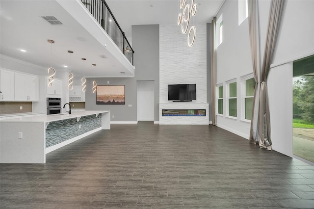 unfurnished living room with a towering ceiling, dark wood-type flooring, a fireplace, crown molding, and sink