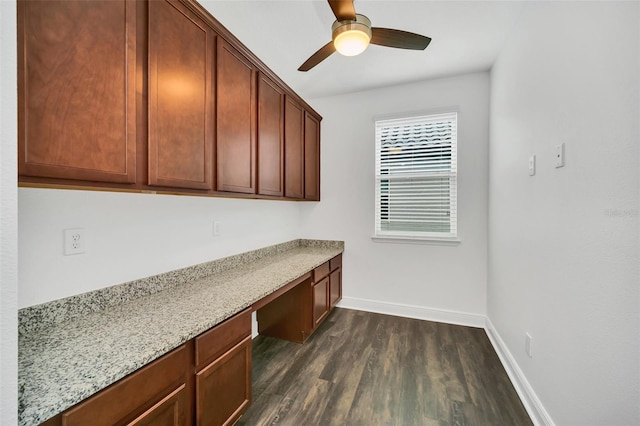 unfurnished office with ceiling fan, built in desk, and dark hardwood / wood-style floors