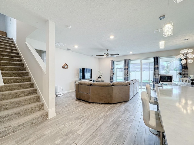 living room featuring light wood-type flooring, ceiling fan with notable chandelier, and a textured ceiling