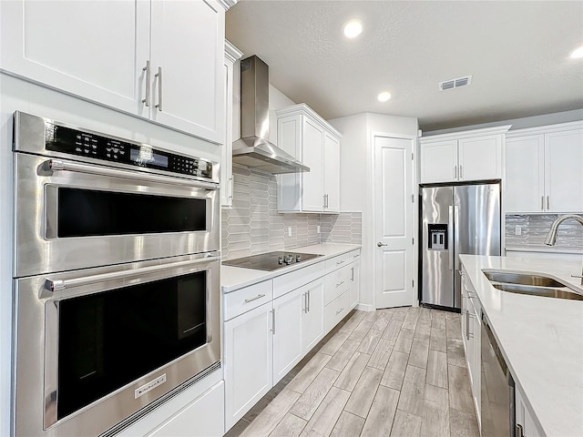 kitchen featuring white cabinets, stainless steel appliances, light hardwood / wood-style flooring, sink, and wall chimney range hood