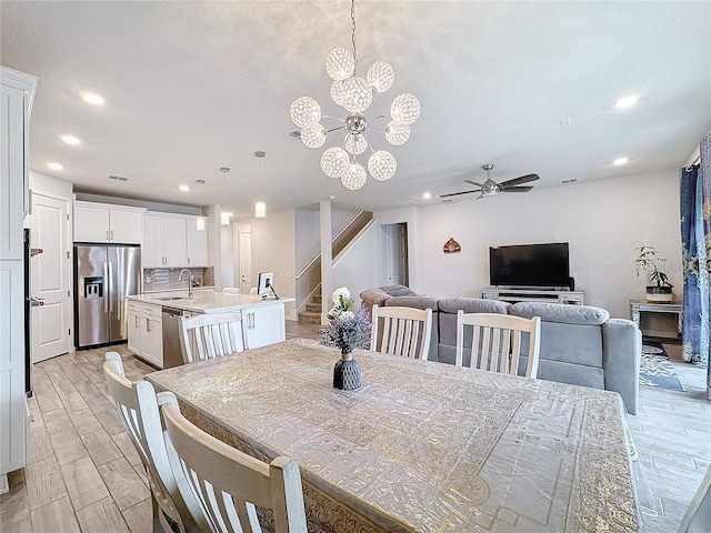 dining room with ceiling fan with notable chandelier, light wood-type flooring, and sink