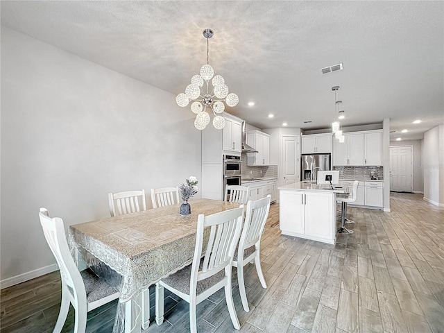 dining room with light wood-type flooring, a textured ceiling, and a chandelier