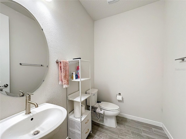 bathroom with wood-type flooring, toilet, sink, and a textured ceiling