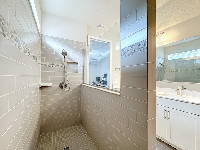 bathroom with tile walls, a textured ceiling, vanity, and tiled shower