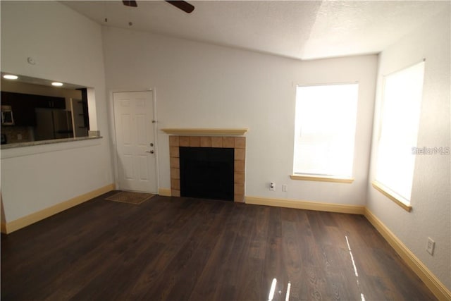 unfurnished living room with a tiled fireplace, dark wood-type flooring, a textured ceiling, high vaulted ceiling, and ceiling fan