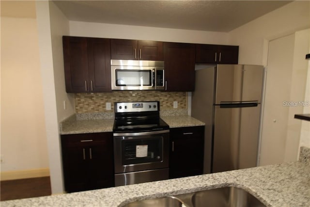 kitchen with appliances with stainless steel finishes, dark brown cabinetry, tasteful backsplash, and light stone counters