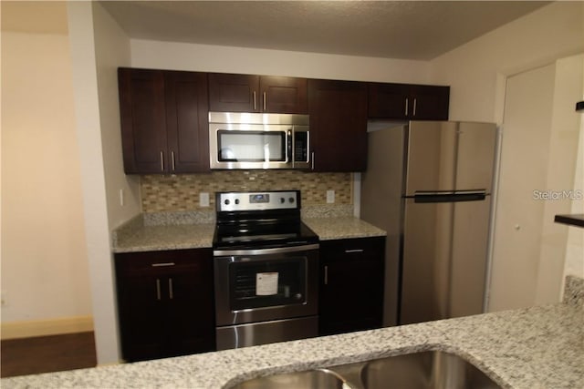 4400 Thornbriar Ln Unit A202, Orlando, FL 32822 - kitchen featuring appliances with stainless steel finishes, dark brown cabinetry, backsplash, light stone countertops, and baseboards