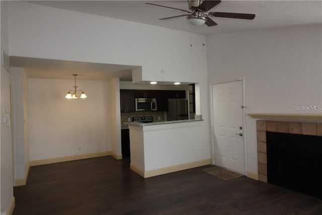 unfurnished living room with a towering ceiling, a fireplace, ceiling fan with notable chandelier, and dark hardwood / wood-style flooring