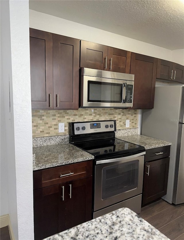 kitchen featuring stainless steel appliances, dark wood-type flooring, light stone counters, and backsplash