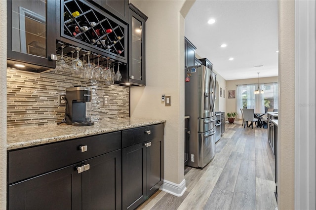 bar with pendant lighting, light hardwood / wood-style flooring, stainless steel refrigerator with ice dispenser, light stone countertops, and decorative backsplash