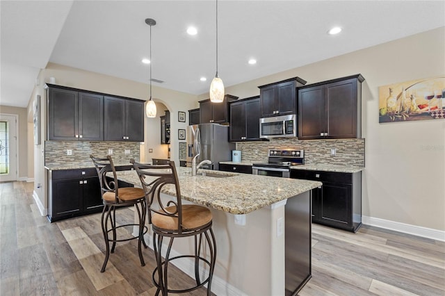 kitchen with a kitchen breakfast bar, light hardwood / wood-style floors, stainless steel appliances, decorative light fixtures, and a kitchen island with sink