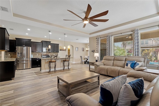 living room with ceiling fan, light wood-type flooring, and a tray ceiling