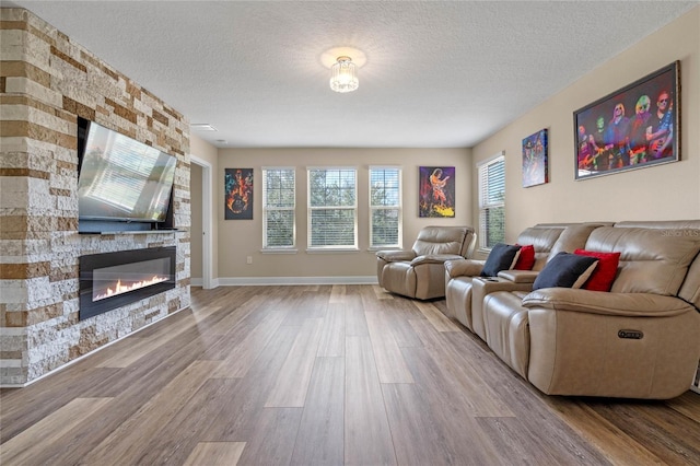 living room featuring a textured ceiling, hardwood / wood-style flooring, and a stone fireplace