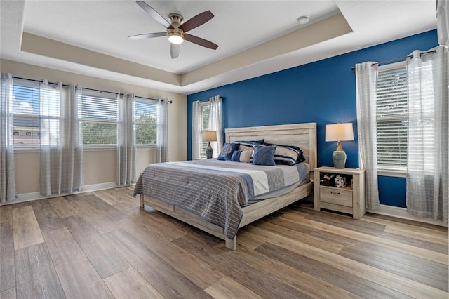 bedroom featuring ceiling fan, wood-type flooring, a tray ceiling, and multiple windows