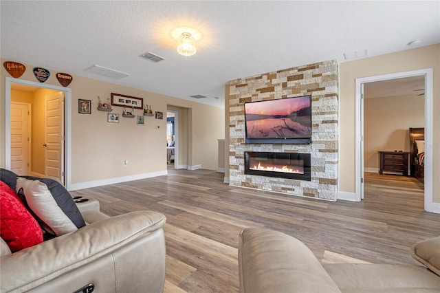 living room featuring a stone fireplace, a textured ceiling, and hardwood / wood-style floors