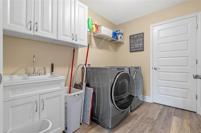 laundry room with cabinets, light wood-type flooring, a textured ceiling, and separate washer and dryer