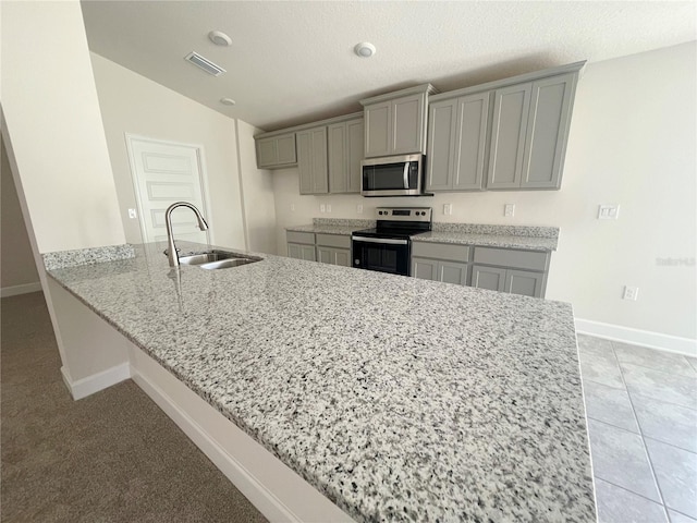 kitchen with appliances with stainless steel finishes, gray cabinetry, kitchen peninsula, sink, and light colored carpet