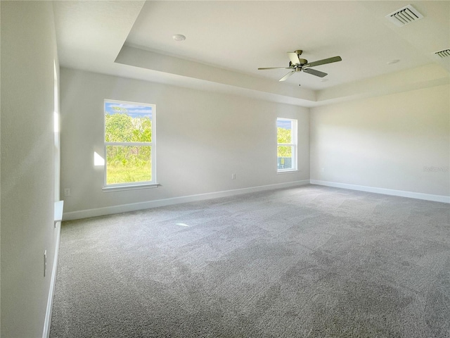 carpeted empty room featuring a tray ceiling, ceiling fan, and plenty of natural light